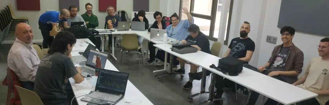 Un montón de gente sentada en círculo en un aula, con múltiples ordenadores liberados con GNU/Linux, dispuestos a arrancar un debate.