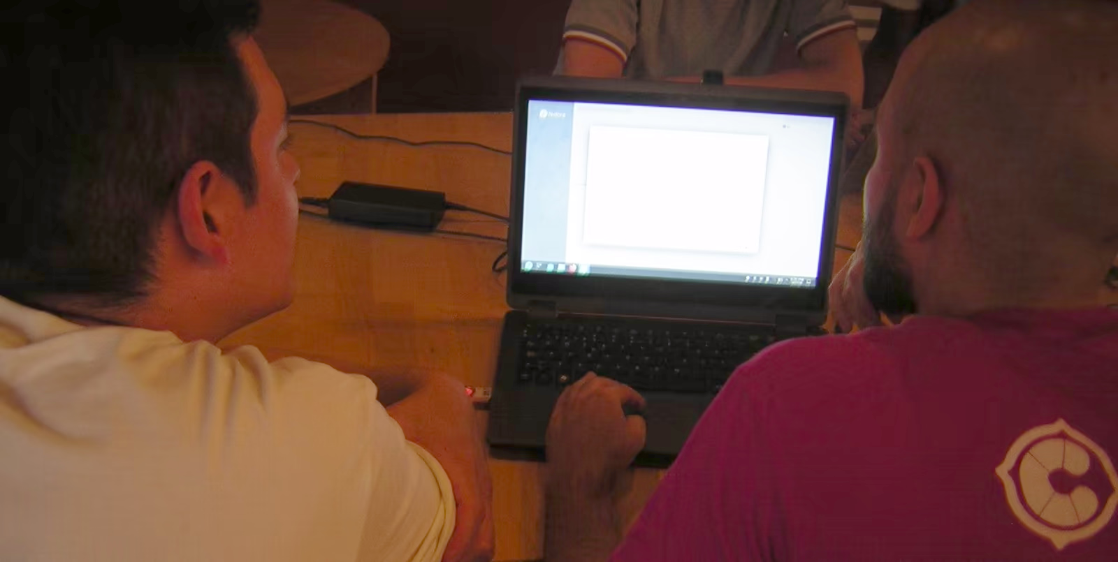 Dos personas frente a un ordenador en el que se está realizando una instalación de GNU/Linux, particularmente Fedora.