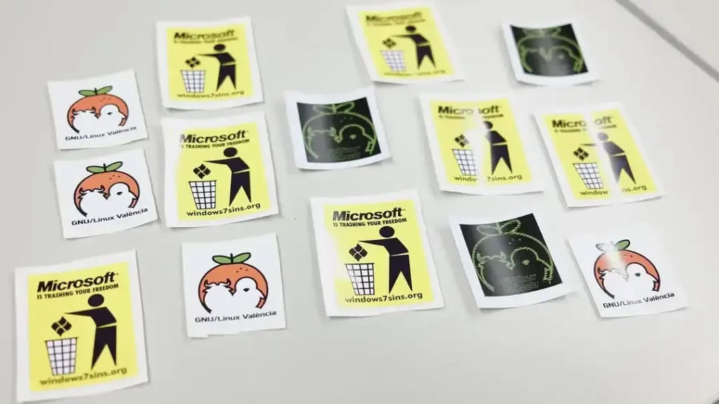 Una mesa sobre la que se encuentran pegatinas de GNU/Linux València y sobre windows7sins.org